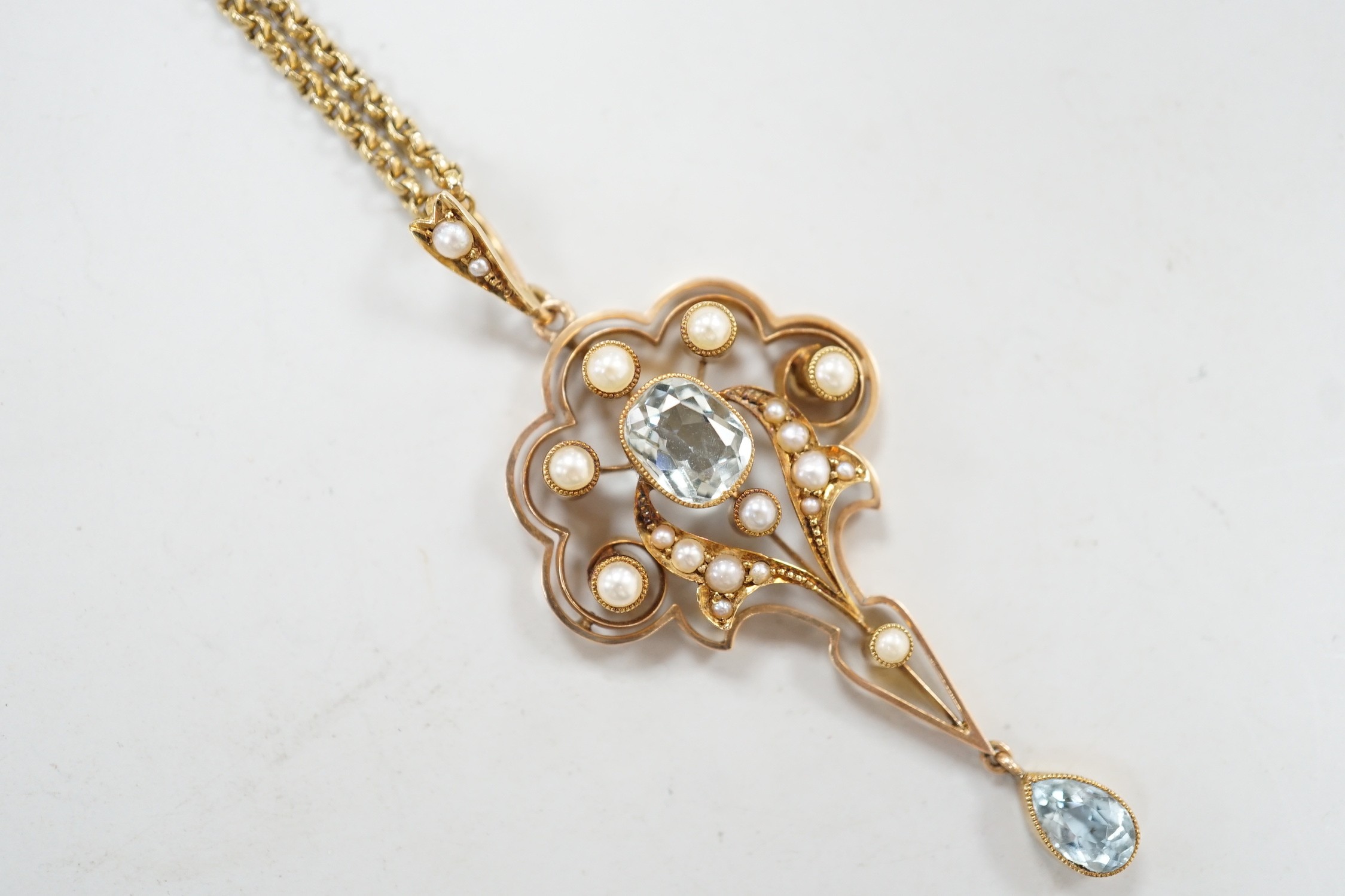 An Edwardian 15ct, aquamarine and seed pearl set drop pendant, 56mm, gross weight 5.3 grams, on a gilt metal chain.